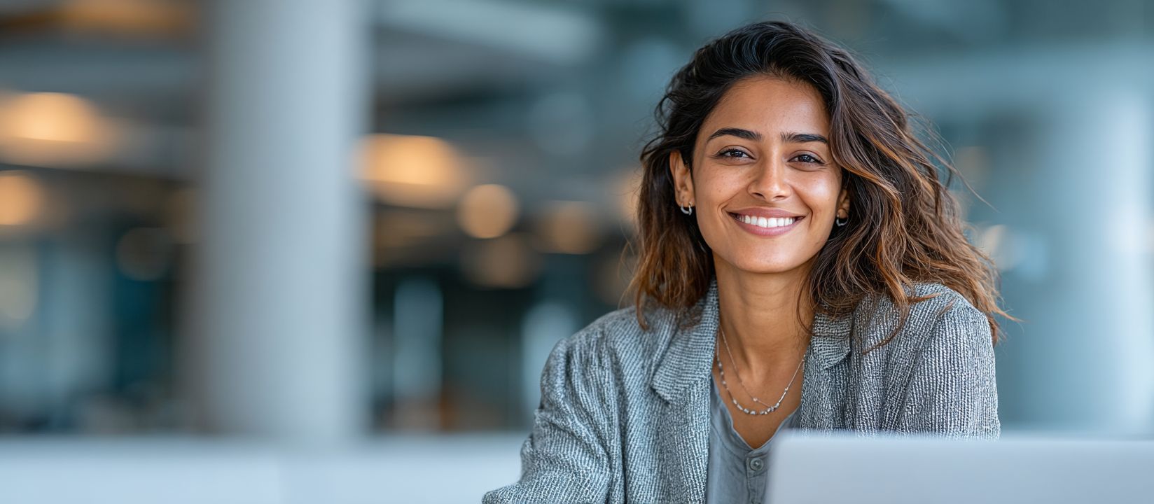 A smiling woman in an office setting with a laptop — enjoy a comfortable gaming experience on Aviator on the 8522 Bet platform from any device